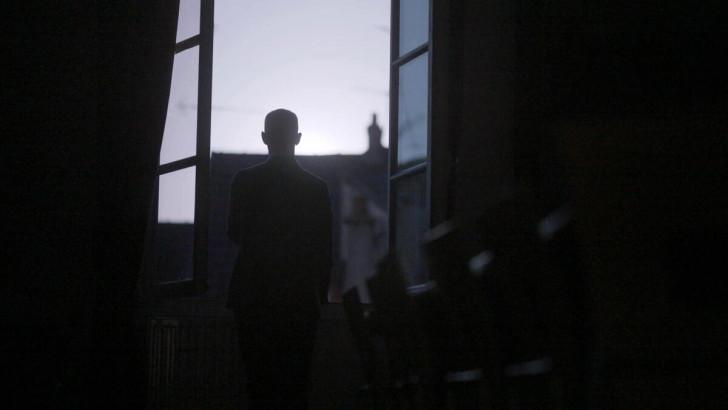 Photo en contre-jour de Franck Riester, de dos, regardant par la fenêtre ouverte